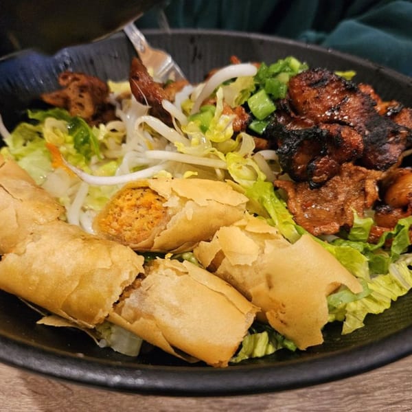 A close-up of a Vietnamese vermicelli bowl with grilled pork, spring rolls, and fresh vegetables.