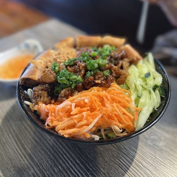 A Vietnamese vermicelli bowl with grilled pork, egg rolls, shredded carrots, and cucumbers.